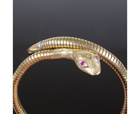 A 9ct gold snake bangle, with ruby eyes and textured engraved head, coiled gold body with steel spring, maker's marks C and F