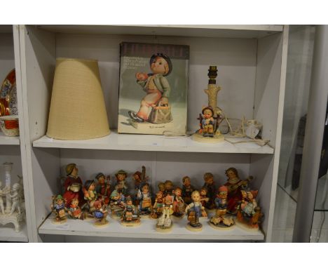 A large collection of Hummel figures, a table lamp and book.