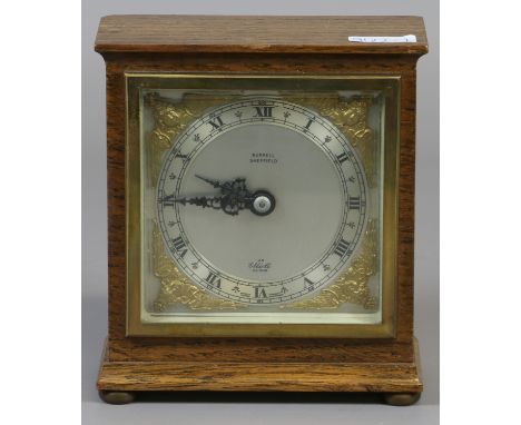 An oak cased Elliot mantel clock with square silvered dial and brass spandrels raised on squat bun feet.