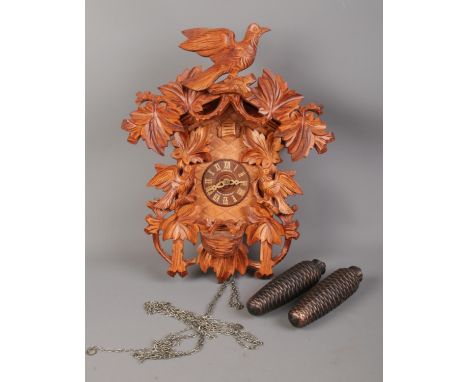 A carved German Schneider Cuckoo clock. H: 42cm W: 34cm.  Missing pendulum. Comes with two weights, will need attention.