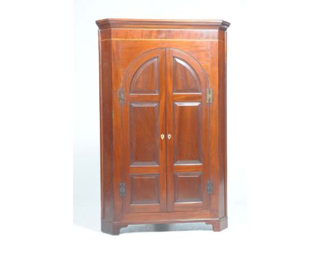 A George III mahogany freestanding corner cupboard
With a moulded cornice above a crossbanded and inlaid frieze over a pair o