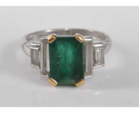 An 18ct white gold, emerald and diamond five stone ring, featuring a centre step cut emerald in a yellow claw setting, flanke