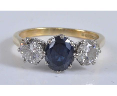 An 18ct yellow and white gold, sapphire and diamond three stone ring, featuring a centre oval faceted sapphire with a round b