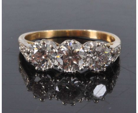 A yellow and white metal diamond three stone ring, featuring three graduated round brilliant cut diamonds in claw settings, d