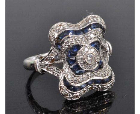 A white metal, sapphire and diamond cushion shaped cluster ring, featuring a centre round brilliant cut diamond within a halo