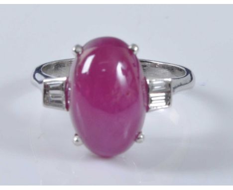 A white metal, ruby and diamond ring, comprising an oval cabochon cut ruby in a four claw setting with two baguette cut diamo