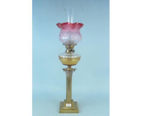 A large size solid brass oil lamp with decorative column and cranberry glass shade 79cm tall, as found to shade