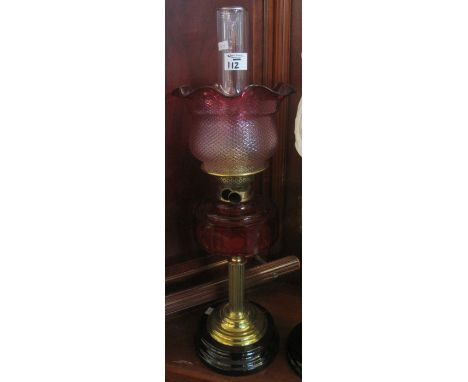 Late Victorian brass double burner oil lamp with cranberry glass reservoir, reeded brass column on ceramic base, graduated cr