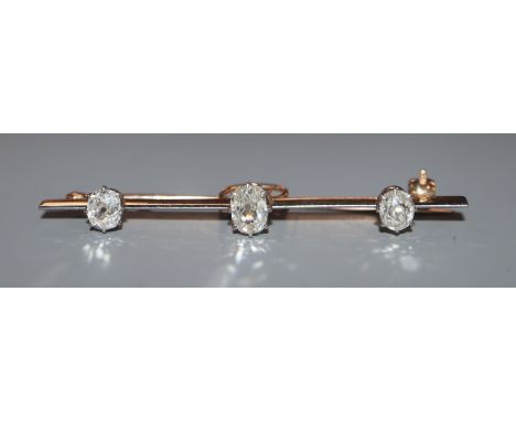 An early 20th century yellow metal and three stone oval cushion cut diamond set bar brooch, 52mm.