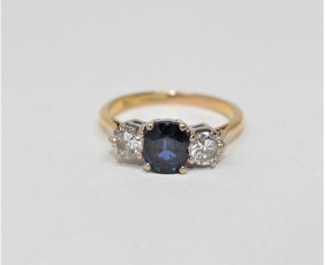 An 18ct gold sapphire and diamond three stone ring, a cushion-cut sapphire in four claw setting between two brilliant-cut dia