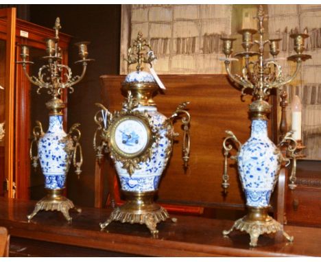 A reproduction Delft style clock garniture, comprising of mantle clock and pair of matching candelabra, decorated with gilt m