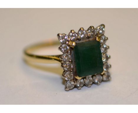 An 18ct gold emerald and diamond ring, the central baguette cut emerald, surrounded by 18 round cut diamonds (approx .54ct in