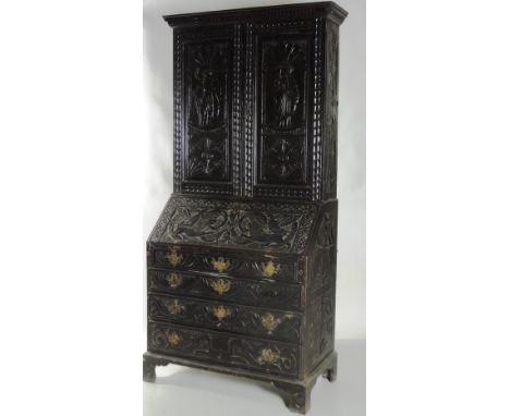 An unusual early 19th Century oak Bureau Bookcase, the two door top profusely carved with two tribal figures over a drop fron