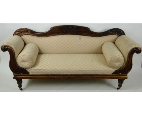 A Regency mahogany framed and upholstered sofa,having a shaped carved back with rollover arms, raised on carved fluted legs, 