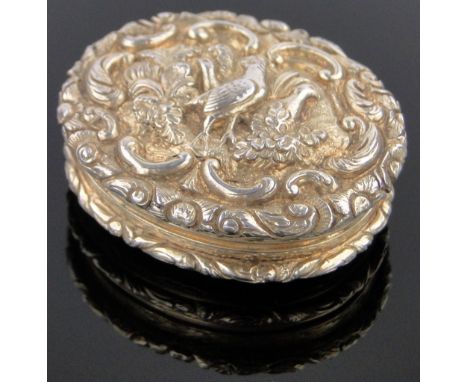 An ornate 19th century unmarked white metal relief decorated oval vinaigrette,with exotic bird decorated lid in scrolled surr