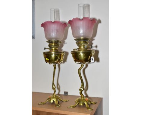 A PAIR OF ART NOUVEAU BRASS OIL LAMPS, clear glass chimneys (not a pair) with reproduction frilled cranberry and white froste