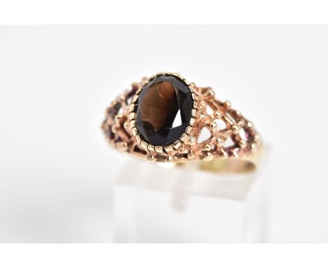 A 9CT GOLD SMOKEY QUARTZ RING, designed with a claw set oval cut smokey quartz and open work detailed shoulders, with a 9ct h