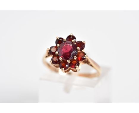 A GARNET CLUSTER RING, designed with a raised cluster set with nine circular cut garnets, to the tapered shoulders, stamped 9