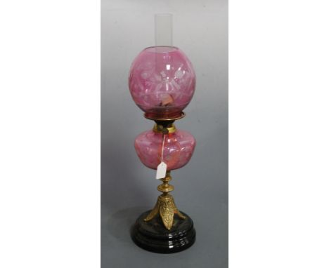 A Victorian oil lamp, having cranberry tinted etched globular shade above a matching cranberry glass font, on embossed brass 