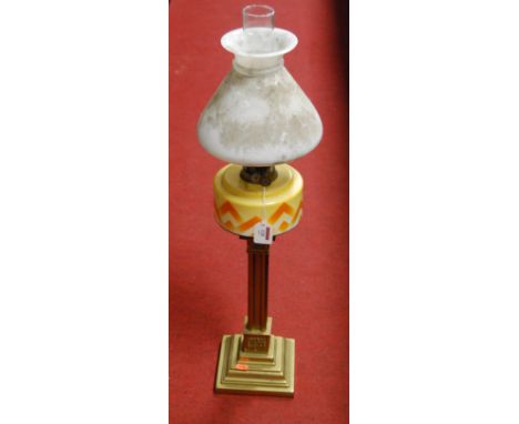 An early 20th century oil lamp, having shaped opalescent glass shade above a yellow and orange glass font, on brass column an