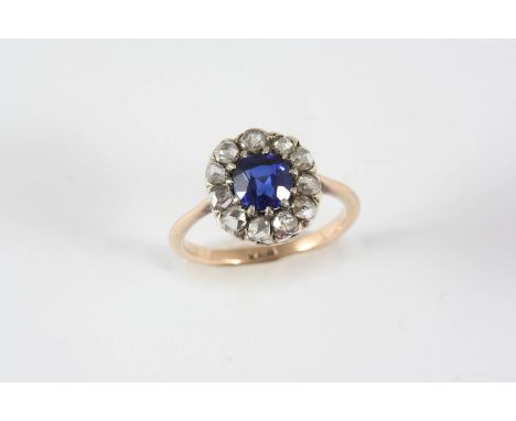 A DIAMOND AND  SYNTHETIC SAPPHIRE CLUSTER RING the circular synthetic sapphire is set within a surround of rose-cut diamonds,