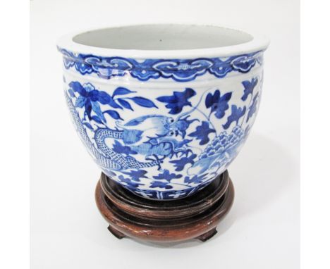 A Chinese blue and white porcelain fish bowl with dragon and leaf decoration on hardwood stand, bearing Kangxi markings but p