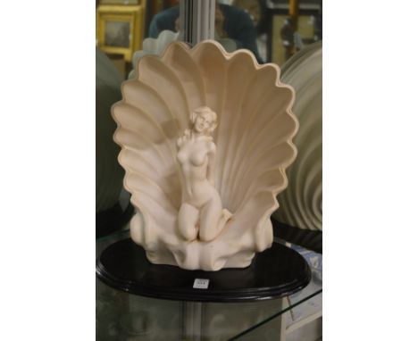 An Art Deco style table lamp modelled as a seated female nude within a shell on a wooden base.