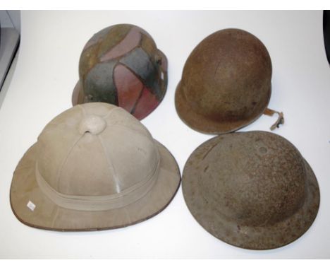 Two German steel helmets together with a British steel Brodie helmet and pith helmet, all as inspected.