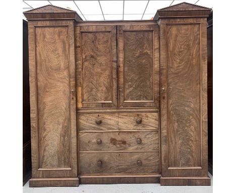 A William IV mahogany wardrobe press, the centre with two figured panel doors enclosing sliding shelves above two short and t