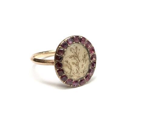 A Georgian gold ring with an amethyst framed panel set with an arrangement of fragments of hair.