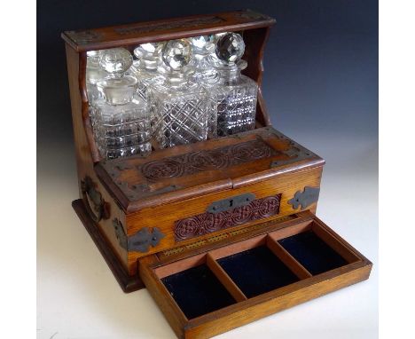 An Edwardian oak three bottle tantalus with games compendium, the carved hinged section opening to reveal liqueur glasses and