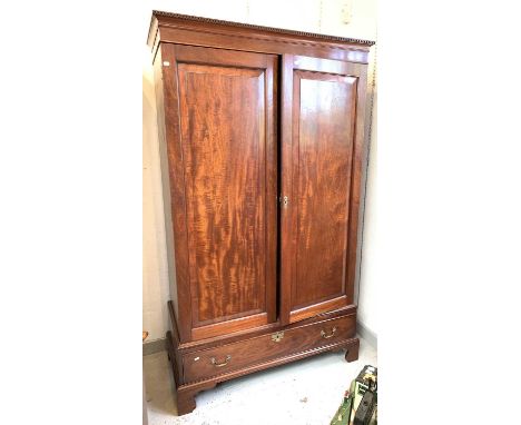 A late George III mahogany wardrobe, with dentil cornice above two figured panel doors, the base fitted one long drawer on br