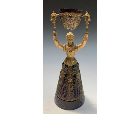 A 19th century continental gilt metal and glass wager cup, modelled as a female in Renaissance style costume, the ruby glass 
