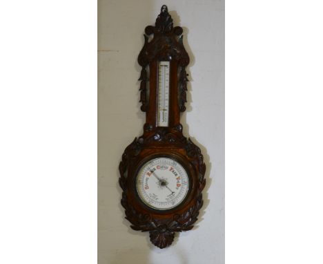 An Edwardian carved oak aneroid barometer, with scrolled bell flower pendants and a wreath surrounding the chart, 23cm.
