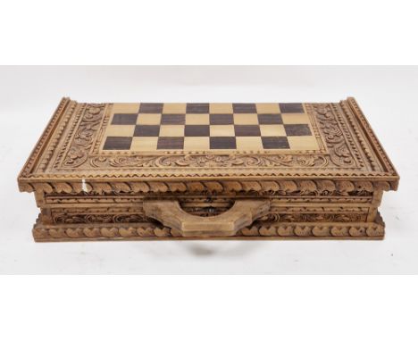 20th century Balinese carved wood chess set, the folding board carved with dense foliage, with carry handles, 42.5cm square