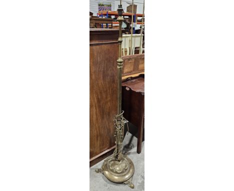Brass aesthetic movement standard lamp, the column cast with scrolls and foliage, on a circular base with three scrolling fee