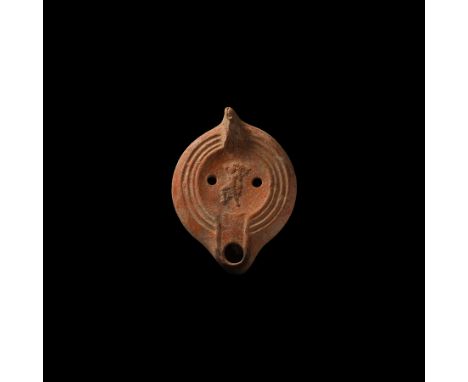 3rd-4th century AD. A terracotta oil lamp with short nozzle and lug handle, the discus with dancer within a concentric circle