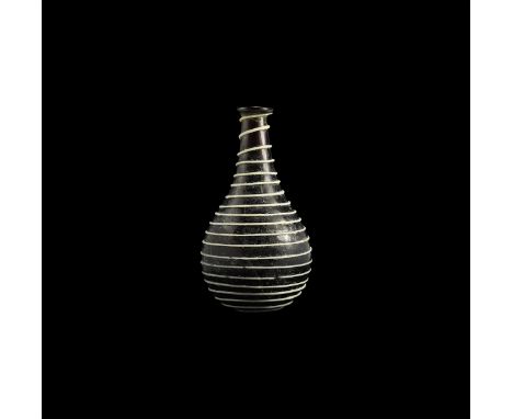 1st century AD. A purple glass piriform bottle with rounded rim and underside, applied white glass trail in spiral to the bas
