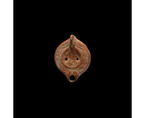 3rd-4th century AD. A terracotta oil lamp with short nozzle and lug handle to the rear; the discus with vine-leaf border, cen