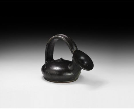 5th-3rd century BC. A ceramic blackware guttos with domed discoid body and central knop to the upper face, broad strap handle