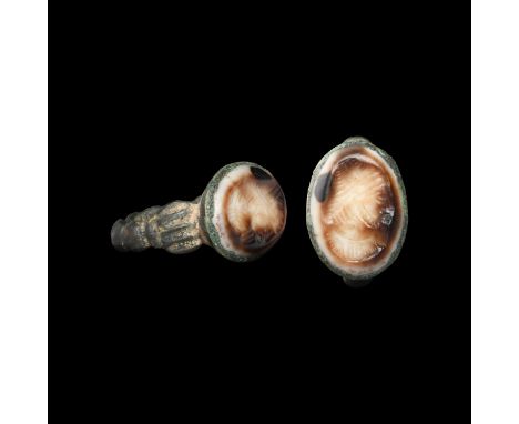 3rd-7th century AD. A silver finger ring with balustered hoop, ribbed plaque to each shoulder, flared bezel with inset sardon
