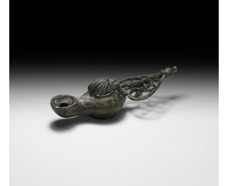 6th-7th century AD. A bronze oil lamp with discoid base, small discoid well and large nozzle with recess to the vent, openwor