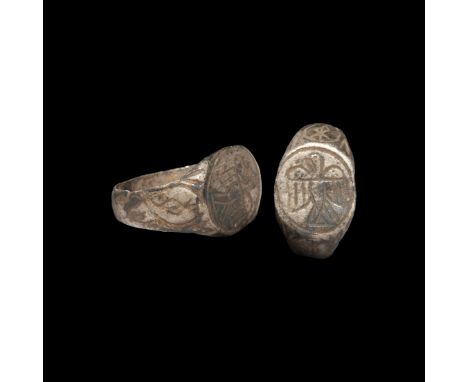 13th-15th century AD. A silver ring with flat-section hoop, scroll motifs to the shoulders, discoid bezel with a splayed eagl
