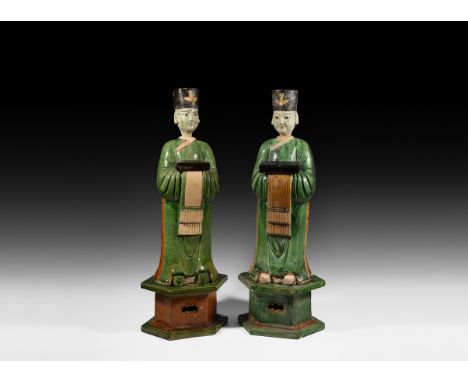 Ming Dynasty, 1368-1644 AD. A pair of ceramic green and brown glazed standing figures each on a hexagonal plinth dressed in f