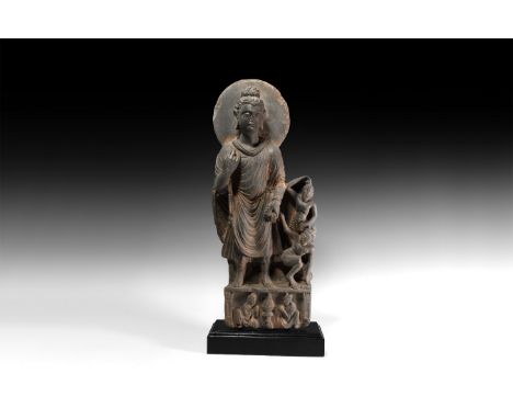 3rd century AD. A schist figure of Buddha standing wearing a loose uttariya garment, right hand raised to the chest and left 