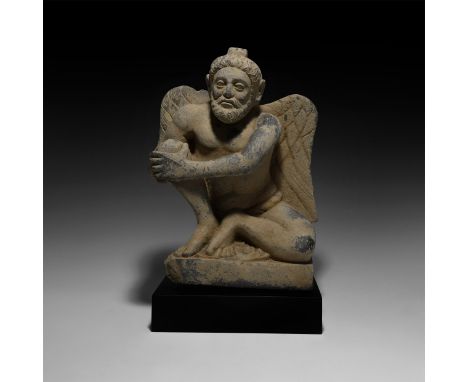 2nd-3rd century AD. A carved schist figure of Atlas crouching with wings partly spread, both hands clasped about his raised r
