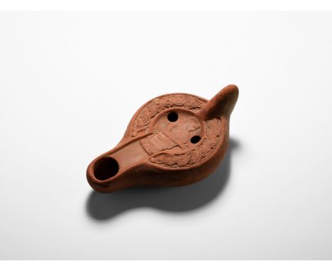 3rd-4th century AD. A terracotta oil lamp with broad discus, lug handle, deep nozzle, applied central profile figure wearing 