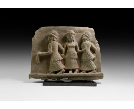 2nd-4th century AD. A carved schist panel with frieze of three dancers, each a youthful female wearing a segmented cap and he