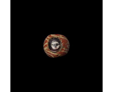 2nd-4th century AD or later. A spherical red glass bead with marvered trail decoration, inset facing mask.   3.3 grams, 13mm 