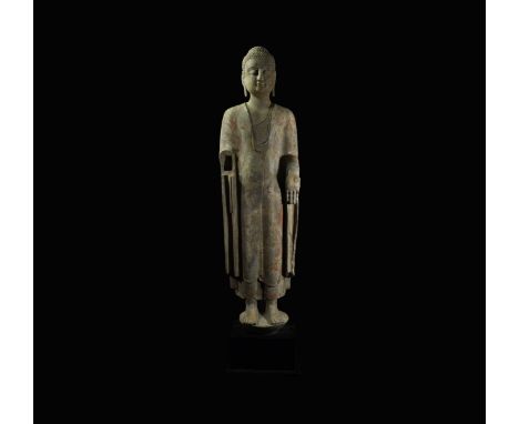 Wei Dynasty, 534-550 AD. A tall stone statue of Buddha standing on a disc base, with hair in tight curls and ushnisha, left h